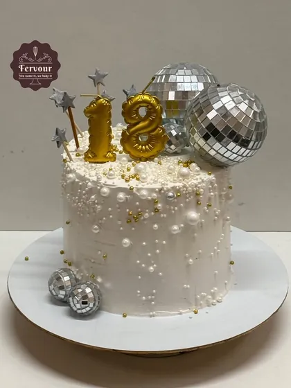 An 18th birthday cake with a disco theme. This white cake is decorated with edible pearls and sparkling disco ball toppers to get the party started.