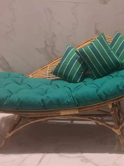 Our elegant rattan chaise lounge, outfitted with a thick, tufted green cushion and matching striped pillows. The curved design provides ergonomic comfort, making it the perfect spot for relaxing indoors or on a covered porch.