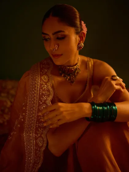 A close-up on the exquisite traditional jewelry and the pop of color from the green bangles against the golden outfit.