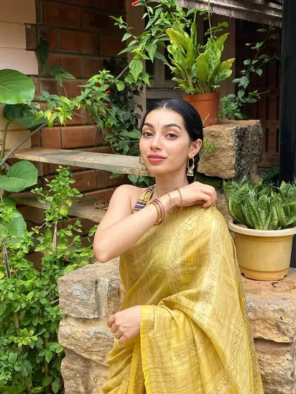 Adjusting my earrings in a candid moment, wearing a lovely yellow saree.
