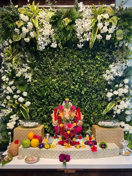 A beautiful Ganpati decoration for the start of your celebrations, featuring a lush green wall and an abundance of white flowers.