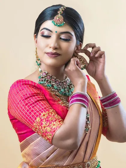 The model adjusting her earring, giving a clear view of the intricate jhumka and the matching maang tikka.