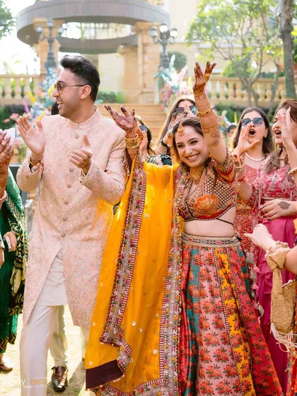 The bride raises her hands in celebration as she and the groom make their energetic entrance to the Mehendi party.