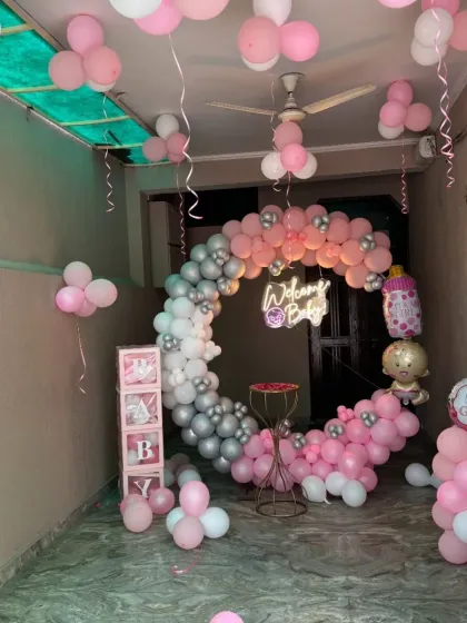 A beautiful "Welcome Baby" setup for a baby girl in a pink, white, and silver chrome color scheme. It features a circular balloon garland, a neon sign, and 'BABY' display boxes, all arranged to create a memorable welcome.