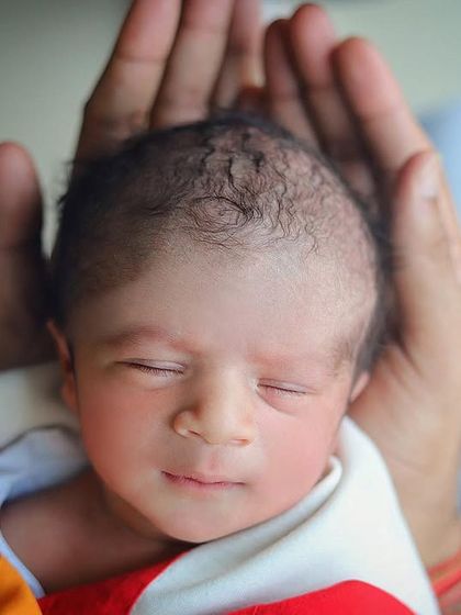 A peaceful newborn portrait, with the baby's head cradled gently in their parent's hands. The focus is entirely on the baby's serene expression.