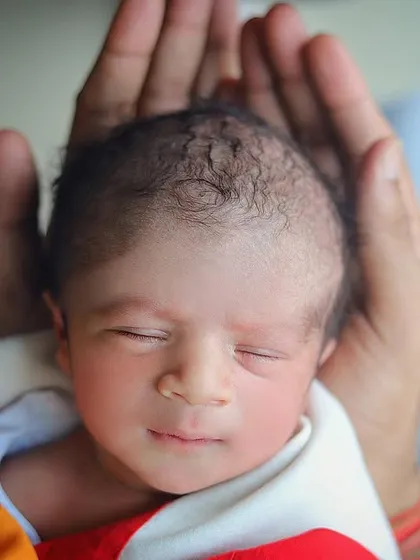 A peaceful newborn portrait, with the baby's head cradled gently in their parent's hands. The focus is entirely on the baby's serene expression.