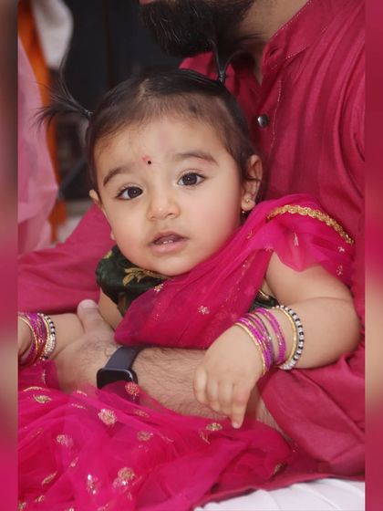 A sweet portrait of a baby girl in a traditional pink lehenga, looking curiously at the camera. This is a duplicate image, emphasizing this popular style.