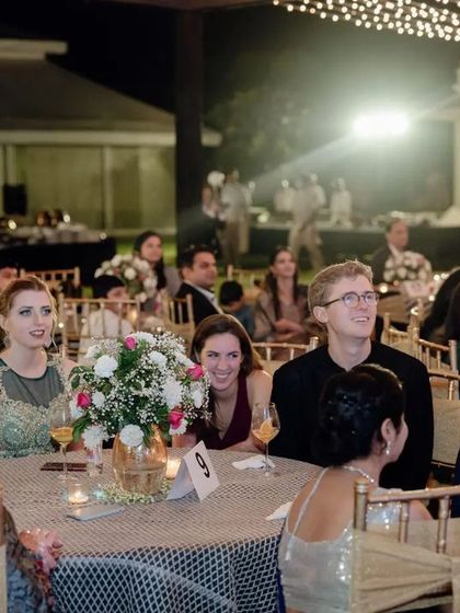 Guests enjoying the reception speeches. The image shows the elegant table settings with floral centerpieces and the warm, inviting atmosphere of the event.