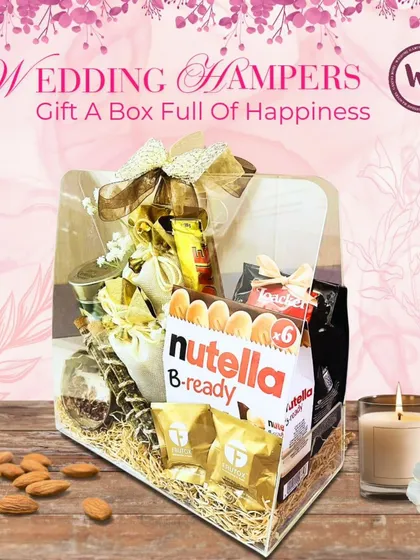 A box full of happiness for the wedding season. This hamper is packed with Nutella B-ready, assorted dry fruits, and other goodies, all presented in a clear box with a beautiful golden bow.