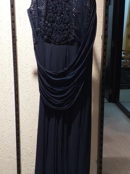 A navy blue draped gown with intricate tonal beading on the bodice. The elegant draping across the waist creates a flattering silhouette for any body type.