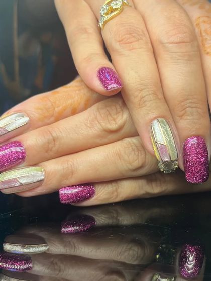 A bold and vibrant manicure with magenta glitter nails and striped metallic accents.