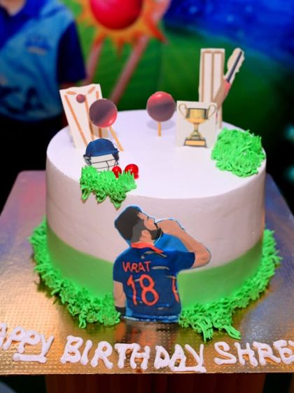 A close-up of the cricket-themed birthday cake. The cake is decorated with edible figures, a trophy, and cricket equipment to perfectly match the party's theme.