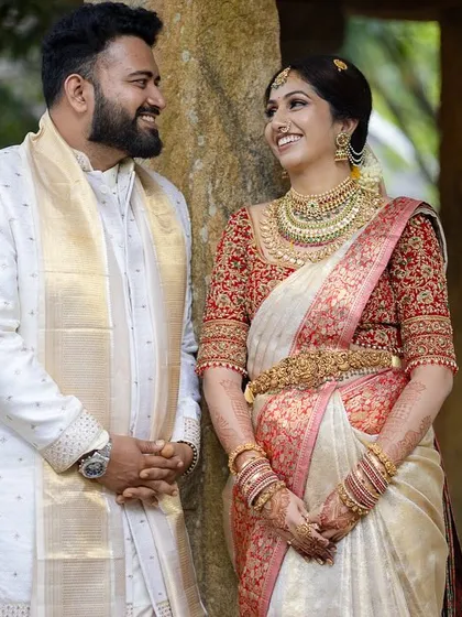 A happy couple poses between the stone pillars of the mantapa, a timeless setting for a classic wedding portrait.