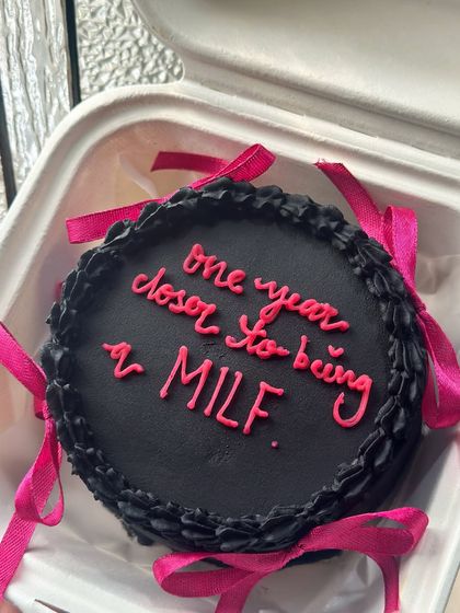 A cheeky black and pink bento cake with satin ribbons. This design is for those who love a bit of playful sass and the trendy coquette aesthetic.