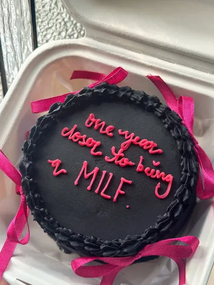 A cheeky black and pink bento cake with satin ribbons. This design is for those who love a bit of playful sass and the trendy coquette aesthetic.