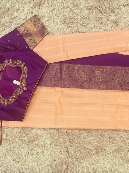 A beautiful pairing of a peach silk saree with a contrasting violet embroidered blouse. The rich jewel tone of the blouse makes the pastel saree pop.