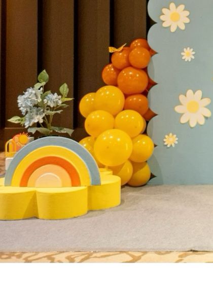 A close-up of a rainbow prop and a balloon cluster, part of the colorful decor for the 'Here Comes the Sun' party.