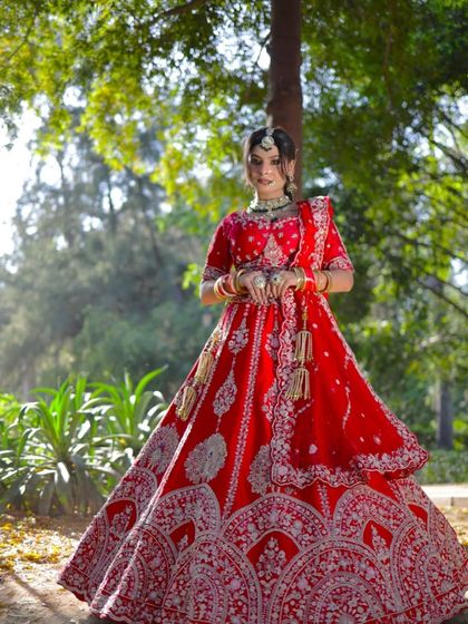 A full view of a stunning red bridal lehenga, perfect for an outdoor wedding. The detailed silver embroidery stands out beautifully against the rich red fabric, creating a timeless and photogenic look.