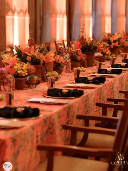 Another view of the long dining table, showing the beautiful contrast between the black napkins and the warm, orange-toned floral arrangements and tablecloth.