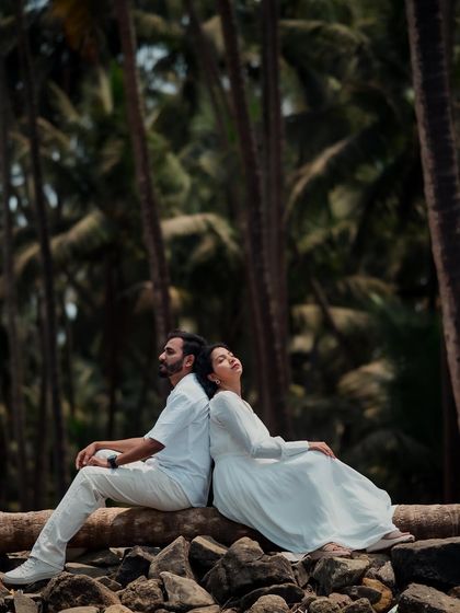 A serene and artistic shot of a couple resting back-to-back on a log. The towering palm trees in the background create a beautiful, natural frame for this peaceful pre-wedding moment.