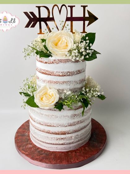 A beautiful two-tiered rustic wedding cake. The "naked" style is adorned with fresh white roses and baby's breath for a simple, elegant look.