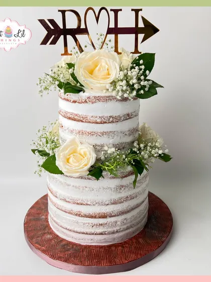A beautiful two-tiered rustic wedding cake. The "naked" style is adorned with fresh white roses and baby's breath for a simple, elegant look.