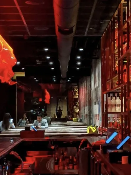 The bar at LokalJC under dramatic red lighting. The custom light fixtures and exposed ductwork contribute to the restaurant's edgy, industrial-chic aesthetic.