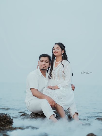 A serene and peaceful moment on the rocks. The couple closes their eyes, enjoying the sea breeze, creating a calm and beautiful photograph.