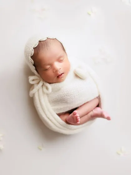 A little miracle in white. This classic pose with a delicate bonnet and wrap shows the baby's tiny feet peeking out, a detail I love to capture.