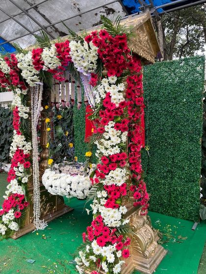 A beautiful cradle for a naming ceremony, fully decorated with red and white flowers. The simple green backdrop ensures that the ornate cradle remains the main focus.