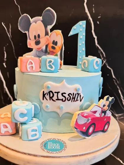 A classic Mickey Mouse themed cake for a first birthday. The design features Mickey and Pluto, along with personalized letter blocks, making it a perfect choice for a little one's special day.