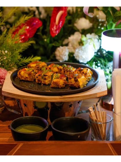 A platter of grilled paneer tikka, served on a miniature sizzler plate. This presentation adds a touch of drama and ensures the dish is served hot and fresh.