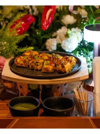 A platter of grilled paneer tikka, served on a miniature sizzler plate. This presentation adds a touch of drama and ensures the dish is served hot and fresh.