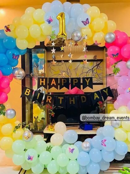 This pastel rainbow ring decoration is perfect for a child's first birthday. The colorful balloons are accented with small butterfly details, creating a gentle and joyful theme for the celebration.