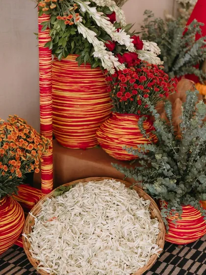Baskets of fresh white petals and colorful striped vases add texture and vibrancy to the Ganesh Pooja decor, showing our attention to detail in every ceremony.