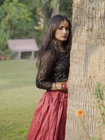 A wider angle of the outdoor fashion shoot, showing more of the green background which contrasts with the model's red and black outfit.