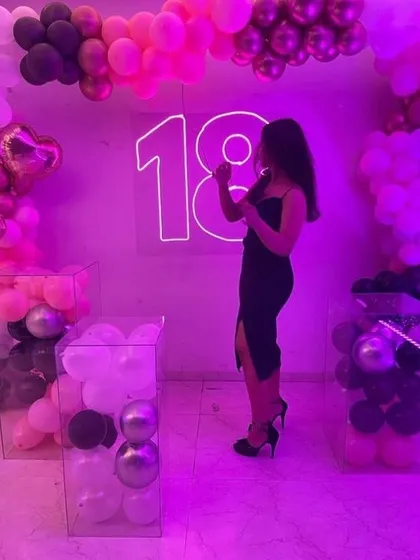 A chic 18th birthday party with a neon pink theme. The setup includes a large neon '18', balloon arrangements, and transparent plinths filled with balloons for a modern touch.