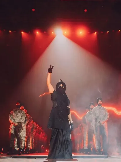 Diljit Dosanjh making a powerful statement on stage. The dramatic spotlight and the formation of his backup performers create a scene of strength and unity.