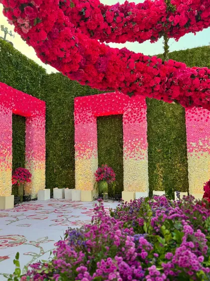 A unique photo-op featuring ombre floral panels and a massive, swirling red floral sculpture, set against a backdrop of green hedges.