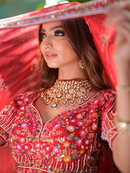 A coy glance from under the veil reveals a stunning polki choker. This image captures the timeless beauty and romance of a bride on her wedding day, enhanced by classic jewellery.