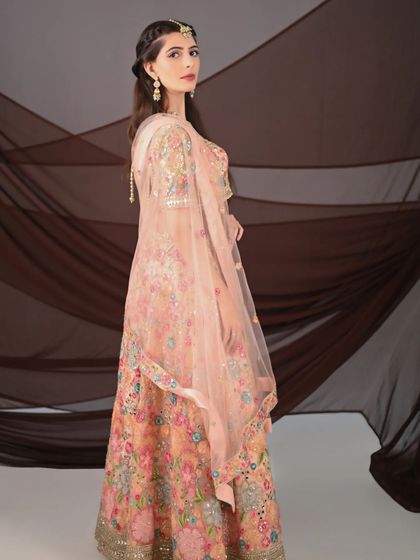 A side profile of the peach floral lehenga, highlighting the intricate, multi-colored threadwork and the delicate net dupatta.