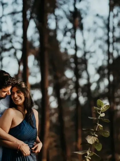 A romantic embrace among the trees near the shoreline. The golden hour light filtering through the branches creates a warm, magical atmosphere for this intimate portrait.