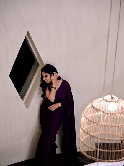 A candid, thoughtful pose in the same purple saree, showing a different mood and expression.