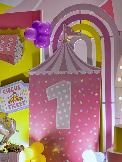 A close-up of a first birthday carnival backdrop. The number '1' is prominently featured on a pink circus tent design, complete with a circus ticket sign, adding to the festive and celebratory theme.