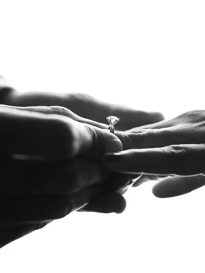 The moment of placing the ring, captured in a stark, high-contrast black and white silhouette that makes the action the absolute focus.