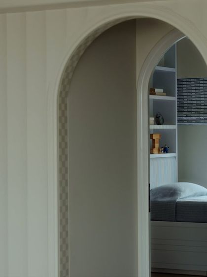 A glimpse through an archway into a child's room, where simple patterns and soft light create a peaceful and playful environment.