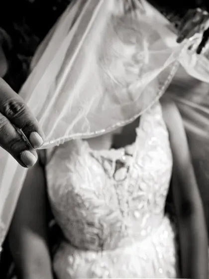 A close-up, black and white shot of the veil being placed, focusing on the hands and the delicate fabric.