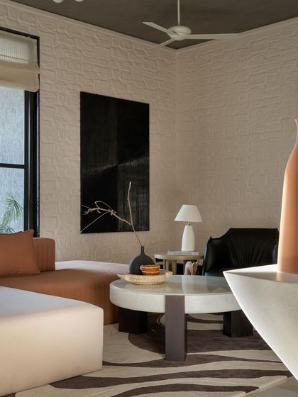 Another view of a living room with a textured wall and a dark, moody painting. The space balances neutral tones with organic elements, with custom furniture crafted for comfort and style.