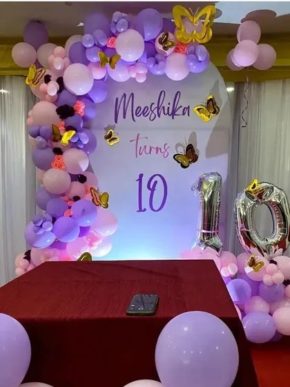 A butterfly-themed 10th birthday party with a purple and pink balloon arch and custom backdrop.