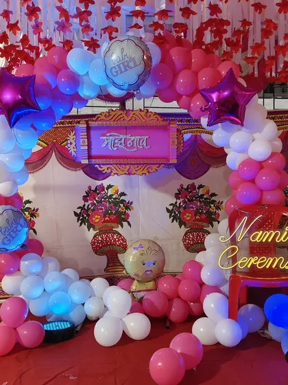 A lovely naming ceremony decoration with a pink and white balloon arch. The setup includes a "Naming Ceremony" neon sign and traditional elements for a blessed occasion.